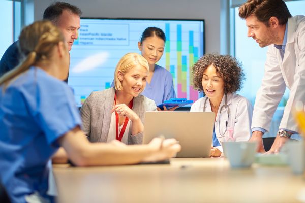 A group of male and female medical professionals crowded together to look at a laptop screen