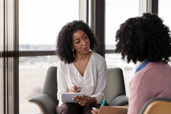 A female sat speaking to another female as she writes on paper