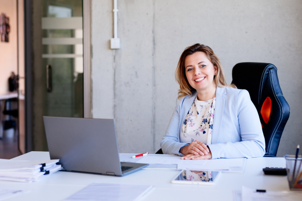 A lady wearing a blue blazer sat at a desk smiling