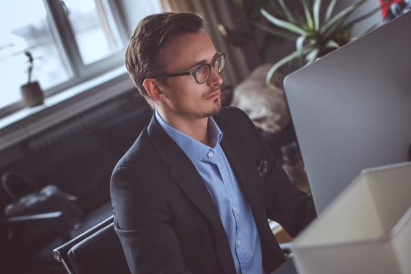 A man wearing a blue shirt and glasses working at his computer