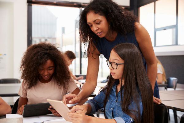 A female teacher showing two female students something on an iPad screen