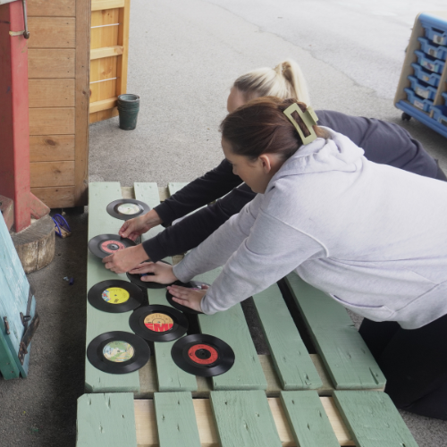 Two Spencer Clarke Group employees building a music wall out of old pallets. 