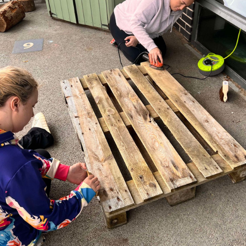 Two employees sanding an old pallet. 