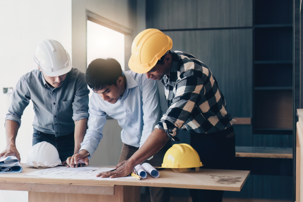 Three men looking at a piece of paper on a table, two are wearing hard hats