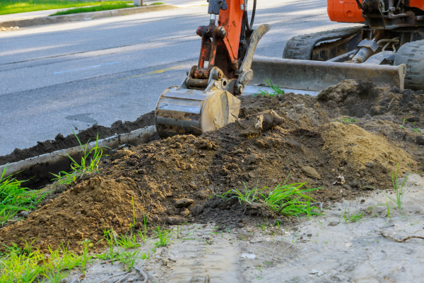 An orange digger moving soil to get to a drain