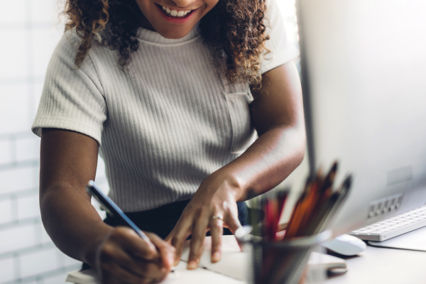 A lady sat at a desk smiling as she writes on paper