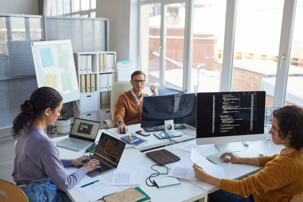 Two men and a lady sat around a desk each looking at an electronic screen