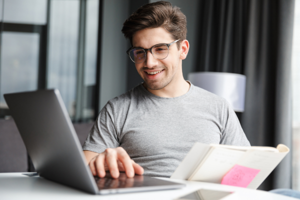 A man wearing a grey t-shirt and glasses looking at a laptop screen