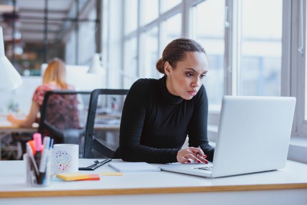 A lady looking at a laptop screen whilst sat in an office