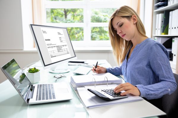 A lady wearing a blue top sat at a desk using a calculator