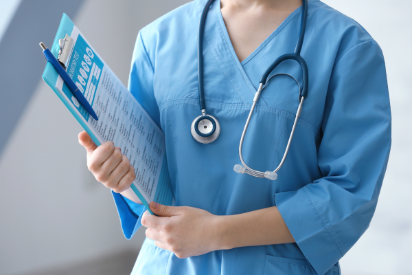 The body of a healthcare professional holding a clipboard while wearing a blue uniform