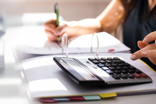 A calculator lying on a notebook with a ladies hand by it