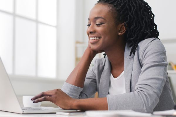 A lady wearing a grey blazer smiling while looking at a laptop