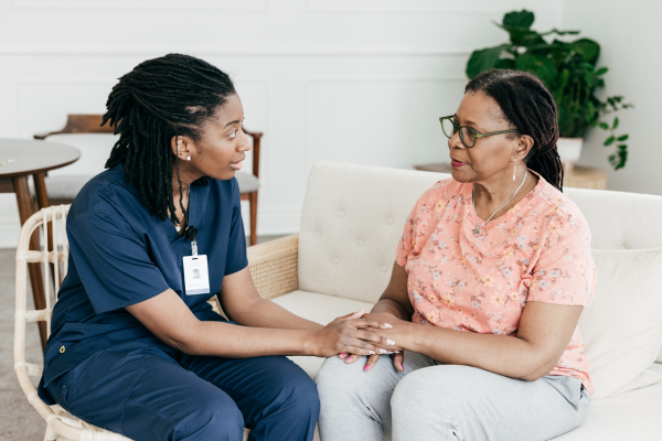 A female Healthcare Assistant sat down holding hands with a female patient