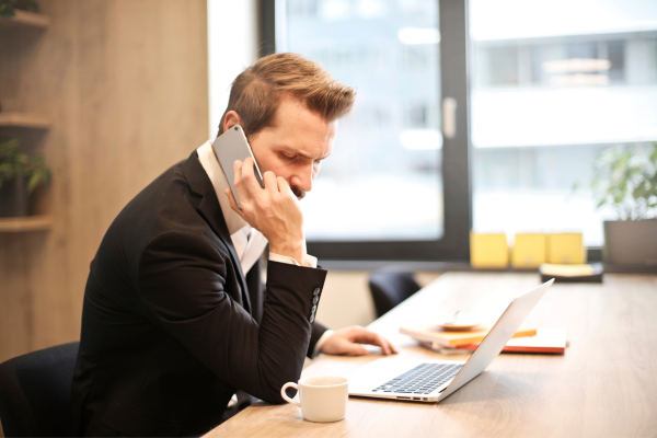 A man wearing a suit sat at a desk on the phone