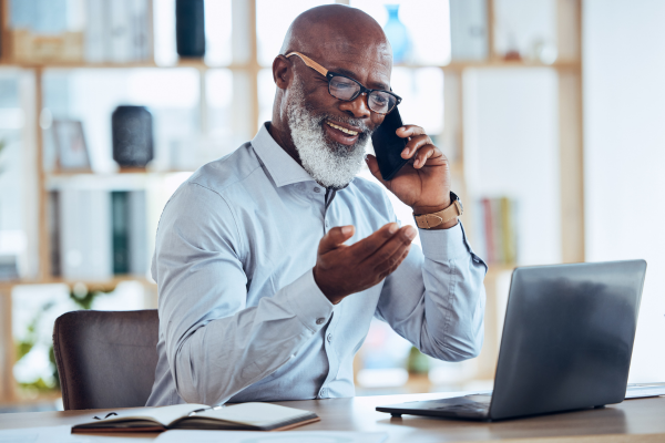 A man wearing a blue shirt and glasses using a phone whilst sat at a desk