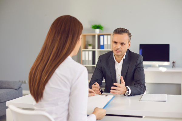 A man in a suit sat talking to a woman on the other side of a desk