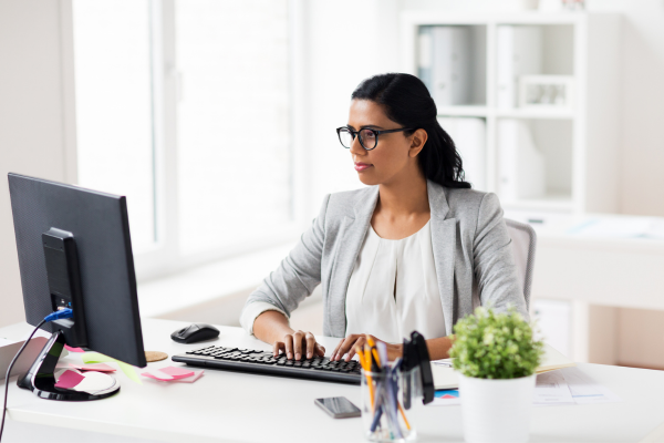 A lady wearing glasses and a grey blazer looking at a computer screen