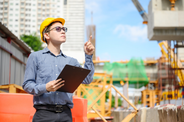 A man wearing a yellow hard hat and glasses pointing at a building