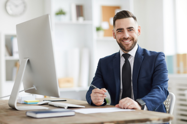 A man wearing a suit sat at a desk holding a pen in his hand