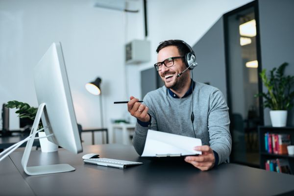 A man sat with earphones on smiling and holding a pen and paper