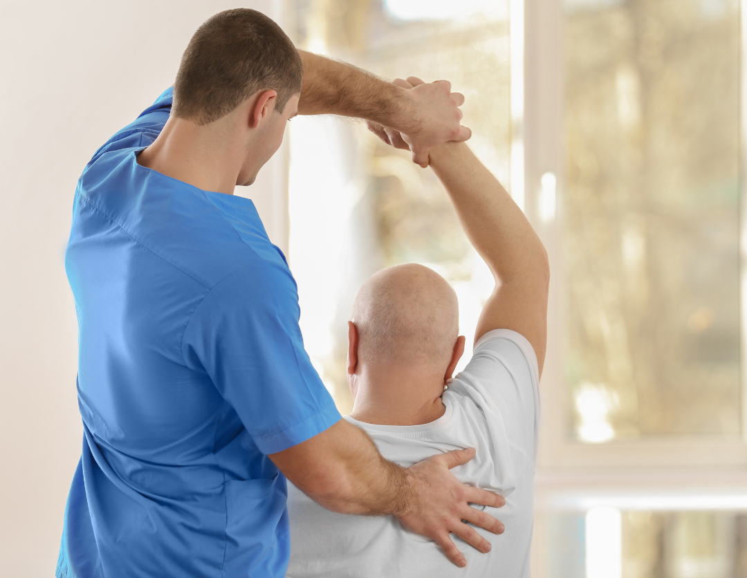 The back of a physiotherapist helping a male patient with stretches