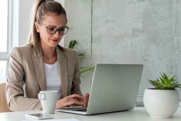 A lady wearing glasses and a blazer typing on a laptop