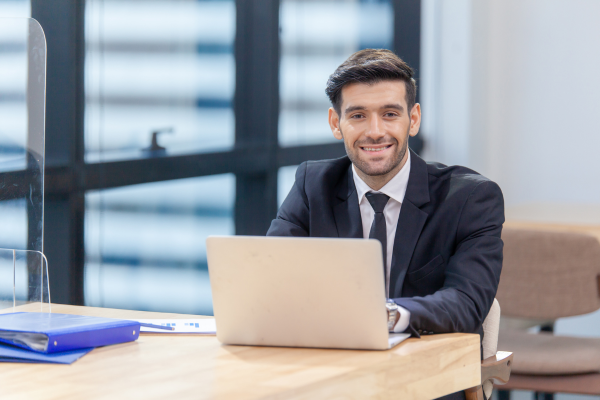 A man wearing a suit sat at a desk with a laptop in front of him