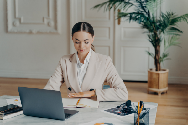 A lady wearing a beige suit sat at a desk looking in a notebook