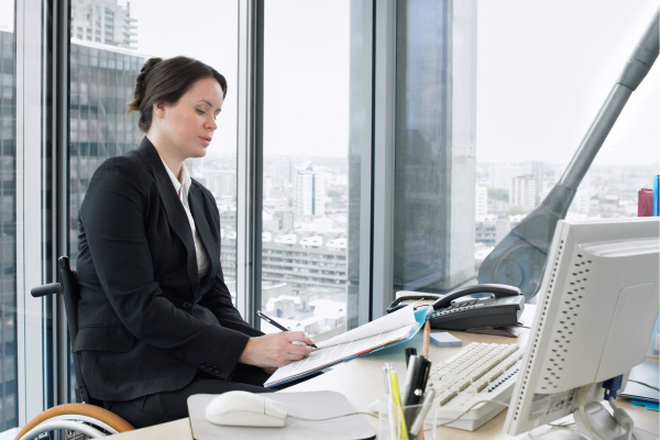 A lady wearing a suit sat at a desk whilst writing in a file