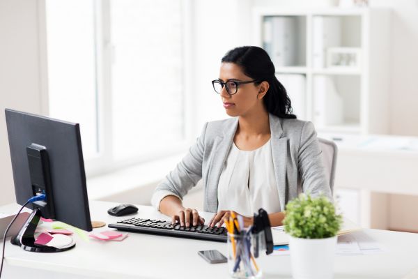 A lady wearing glasses and a blazer sat at a desk using a computer