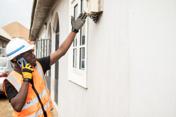 A man wearing orange high vis on the phone whilst checking an electrical appliance