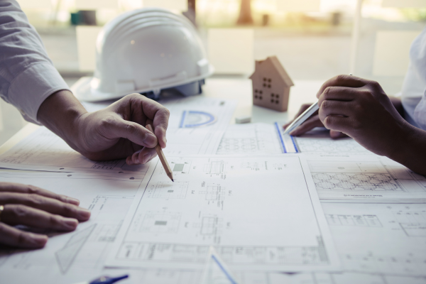 Structural plans laid out on a table with two pairs of hands resting on them