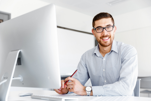 A man wearing a shirt smiling whilst sat at a desk