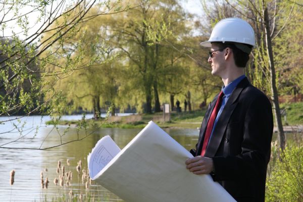 A man wearing a white hard hat outside holding big sheets of paper