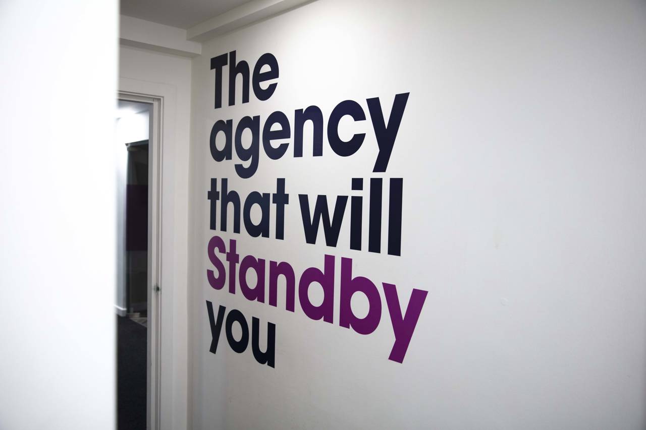 A white wall that has 'The agency that will Standby you' on it