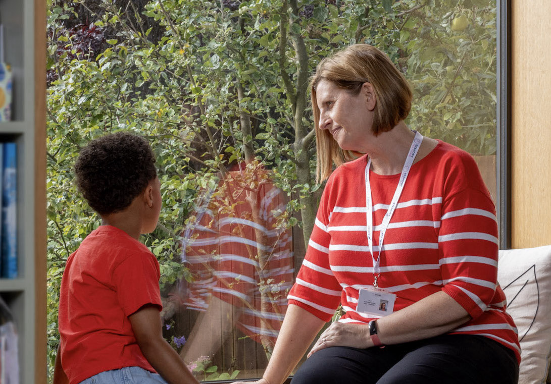 A woman in a red and white striped jumper speaking to a young boy in a red top