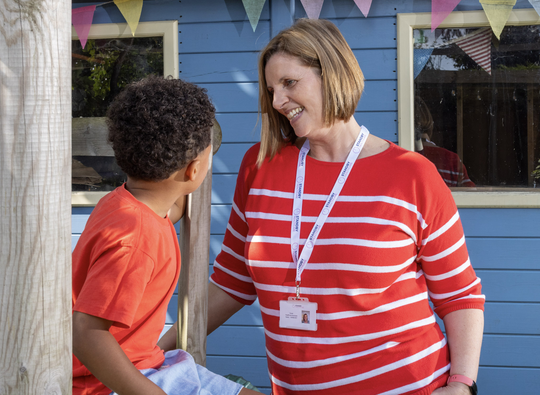 A woman in a red and white striped top, talking to a young boy in a red top on an outdoor play set