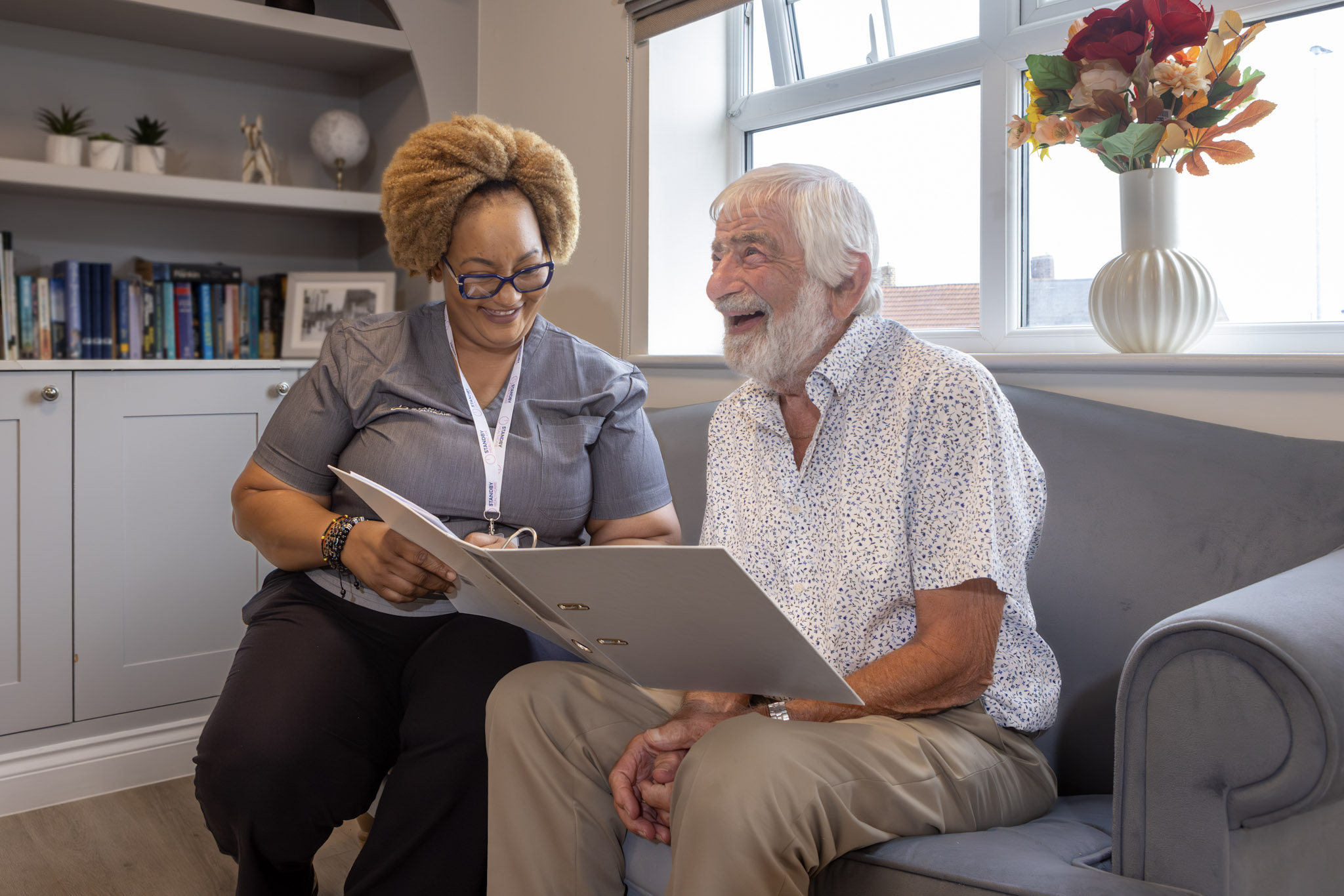 A female care staff member smiling and looking at paperwork with an elderly man
