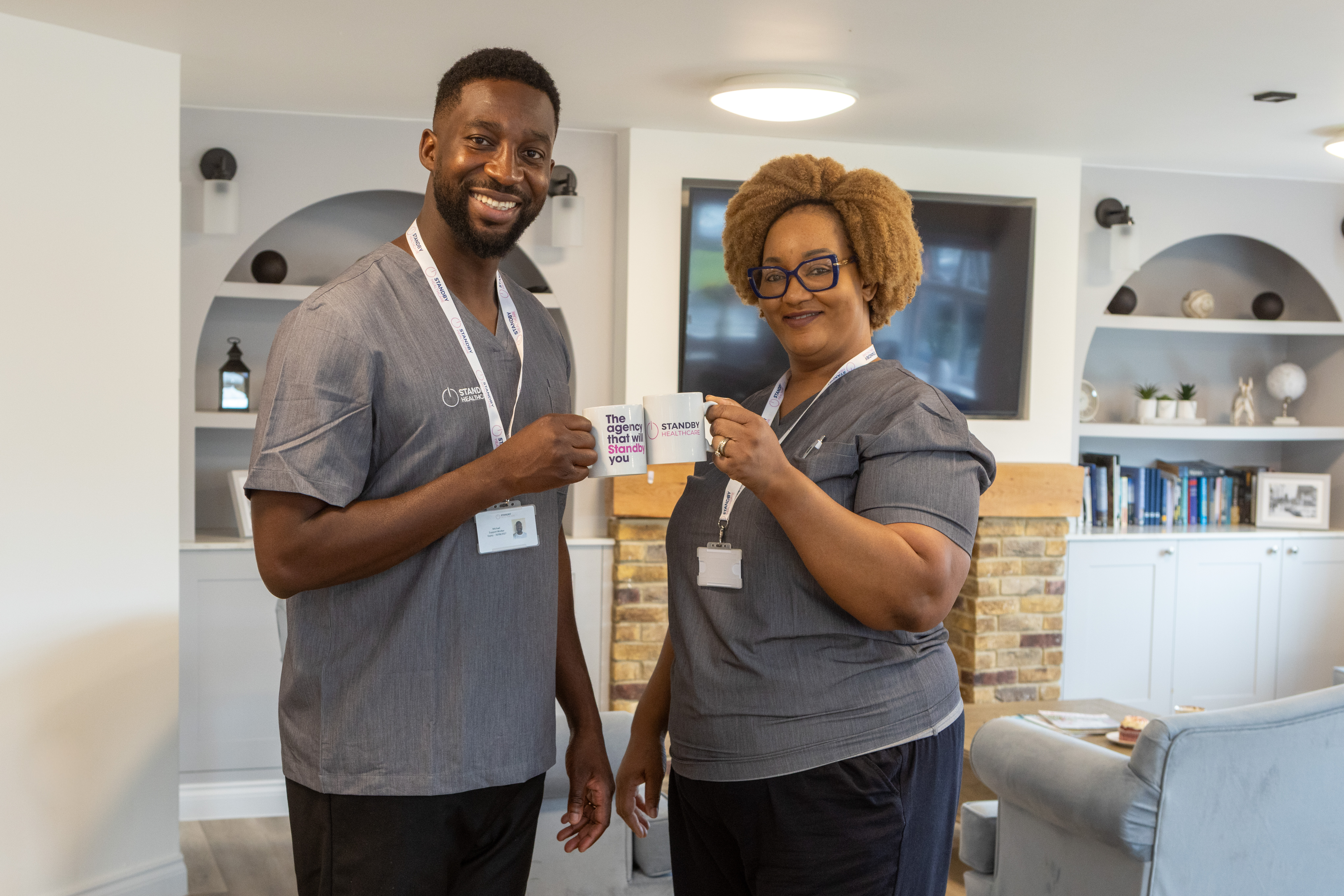 A man and woman in healthcare uniforms holding up Standby Healthcare branded cups