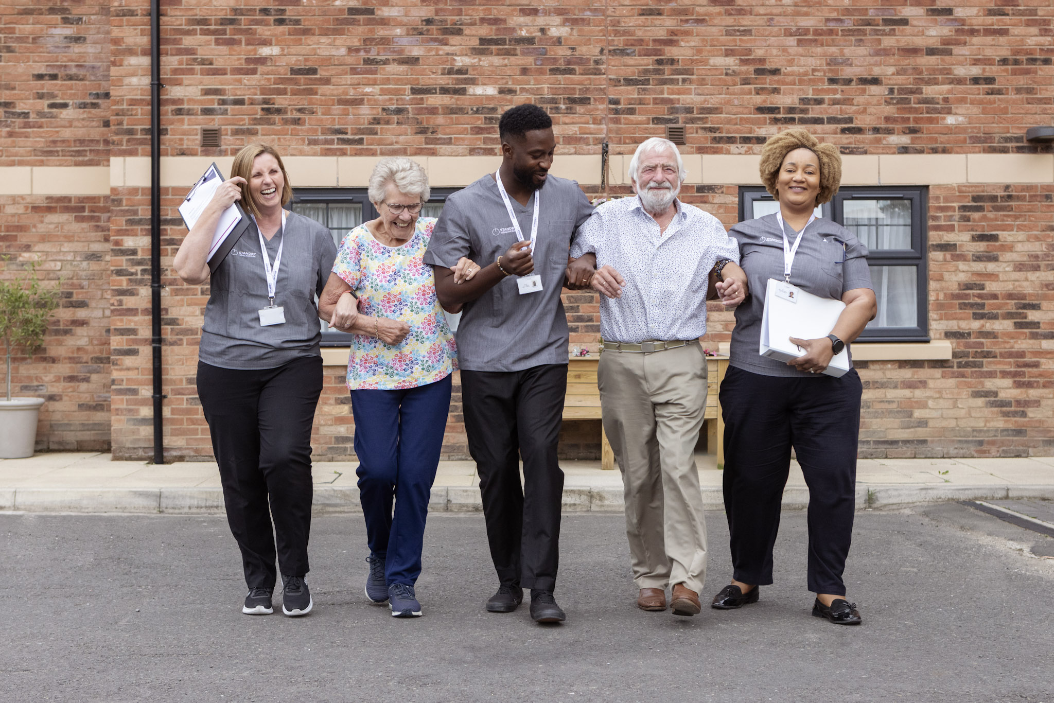 A group of care staff and elderly residents, walking, laughing and smiling with linked arms