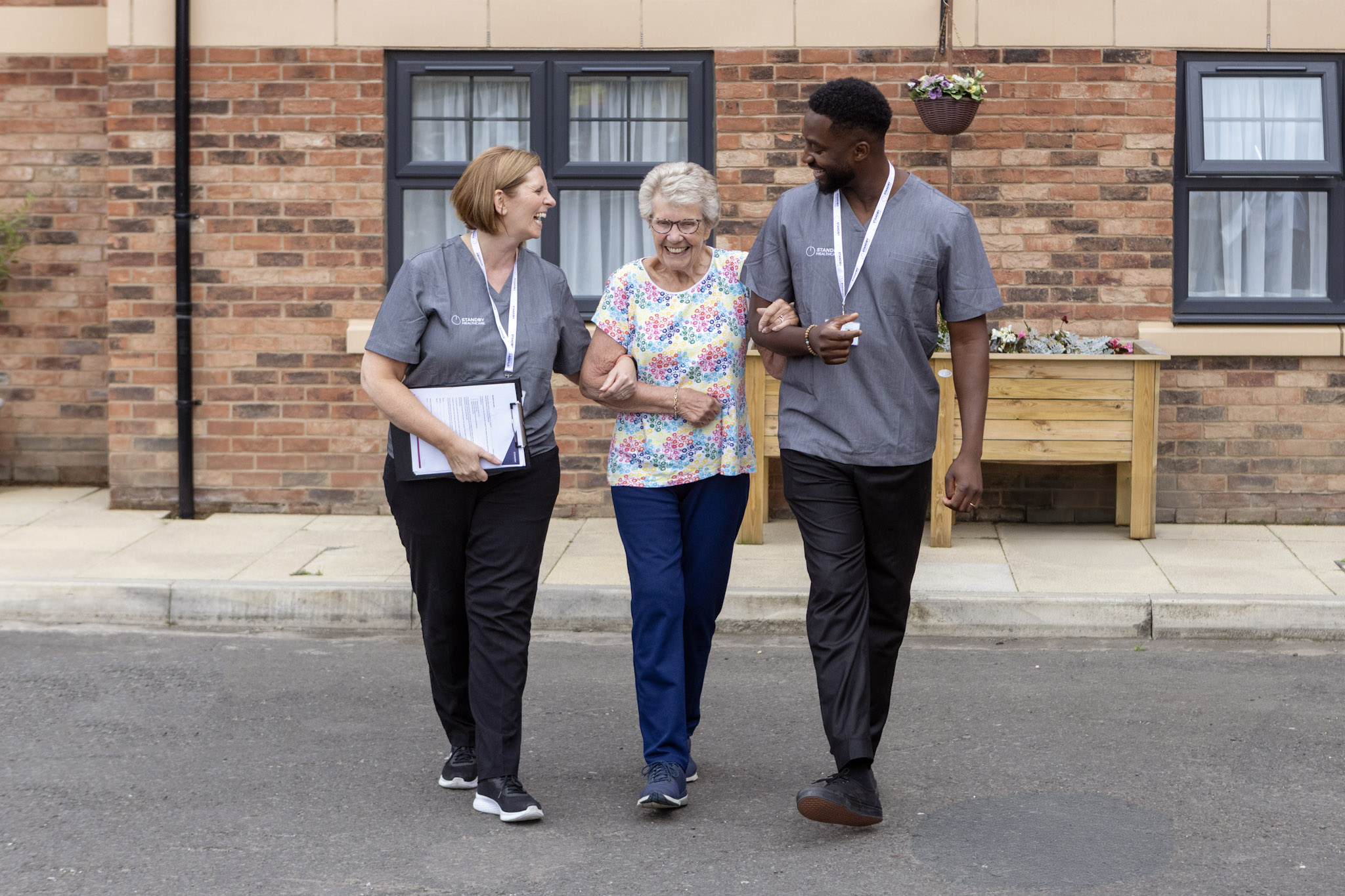 A male and female care staff member helping an elderly woman walk 