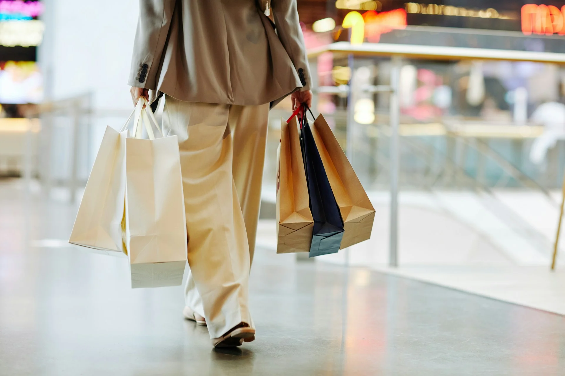 low-section-of-unrecognizable-woman-wearing-pants-and-holding-blank-shopping-bags-while-walking-in-mall-copy-space
