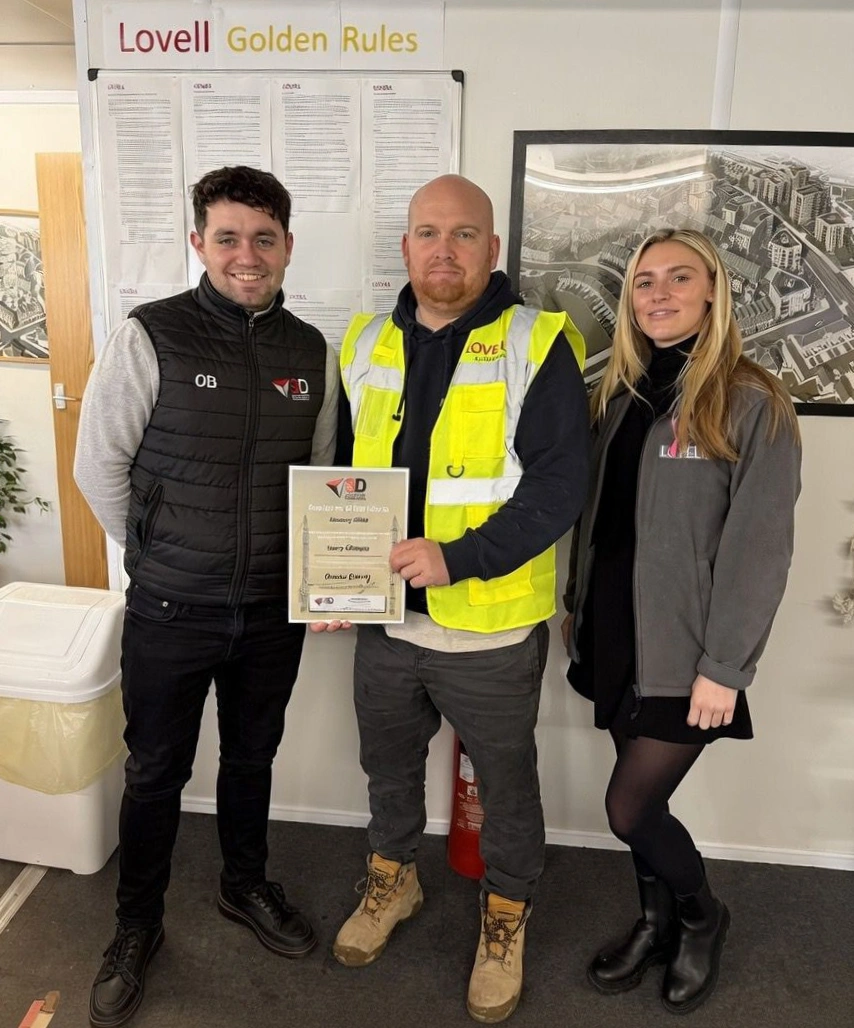 Harry receives his award from Oran and Lily at the site office