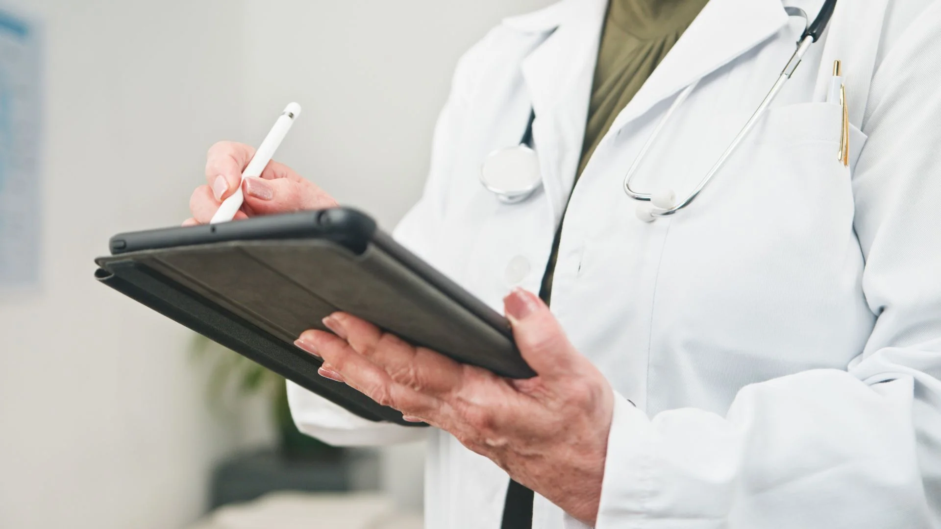 Doctor in white coat with stethoscope using tablet and stylus in medical office setting