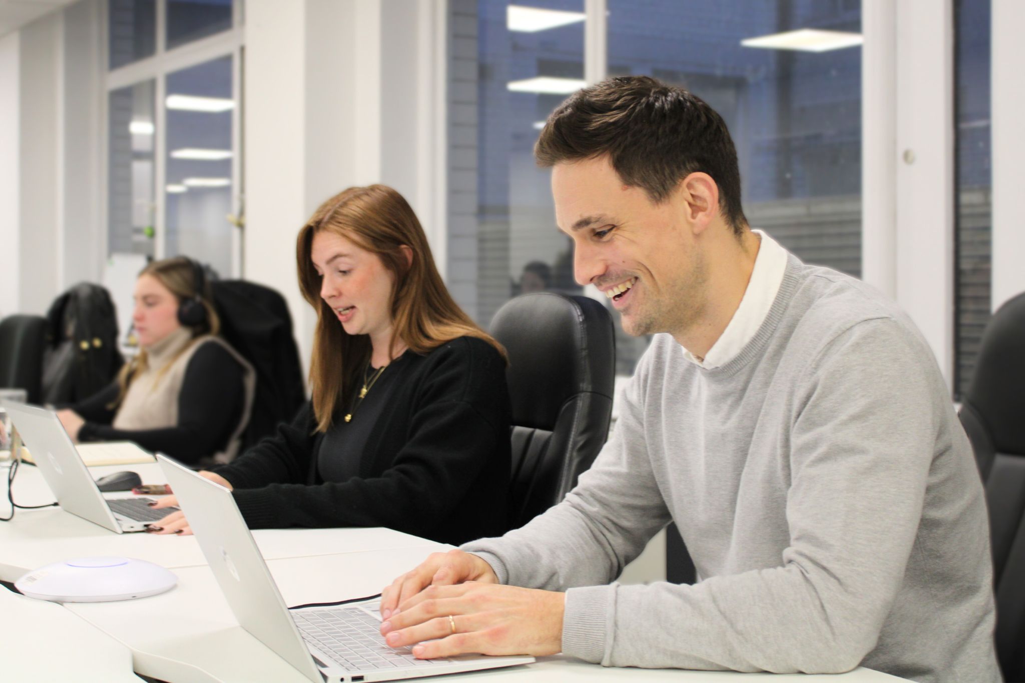 Two headhunters working on laptops, smiling at their screens