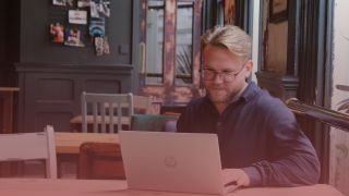 Male recruitment consultant smiling at his laptop as he types. There is a pink overlay on top.
