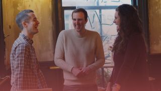 Three recruitment consultants talking together, two men on the left and one woman on the right. There is a pink overlay on top.