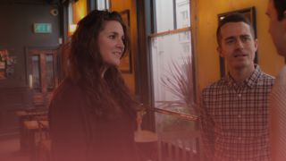 Female recruitment consultant to the left and male recruitment consultant to the right. They're speaking to someone off camera. There is a pink overlay on top.