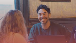 Back of a female recruiter's head to the left and in the centre of the image there is a male recuriter smiling at her.